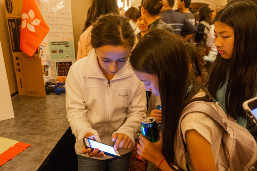 Three young girls looking at a demonstration on a mobile phone.